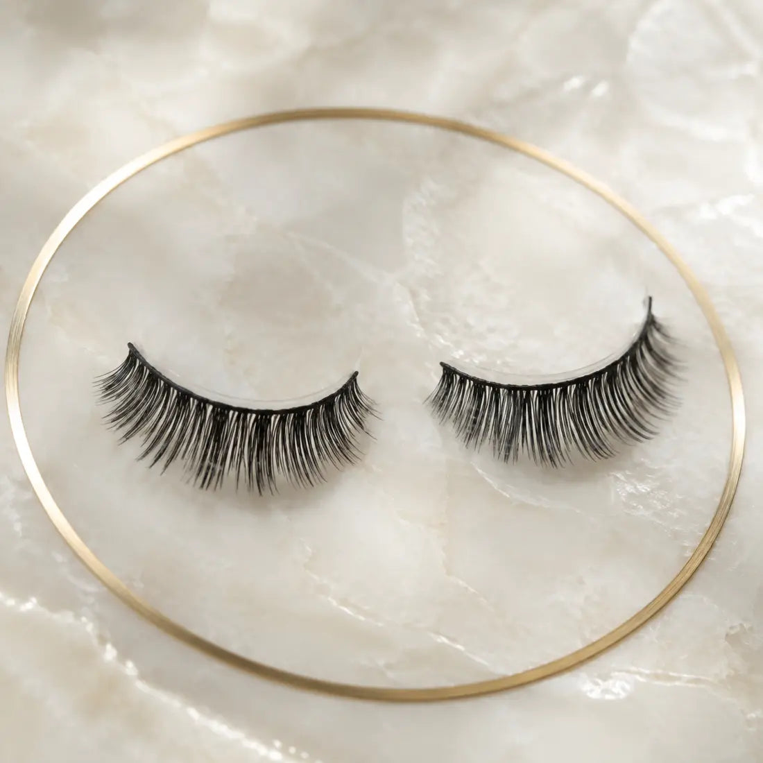 Close view of René magnetic lashes on an ivory surface with a gold ring